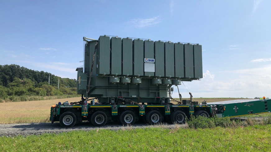 82 Tonnen wiegt jeder der beiden Trafos, die den Solarstrom aus der Freiflächenanlage auf Hochspannungsniveau heben. Die Anlieferung erfolgte auf den letzten Kilometern auf Selbstfahrern, damit sie auf den engen Straßen vor Ort transportiert werden konnten.