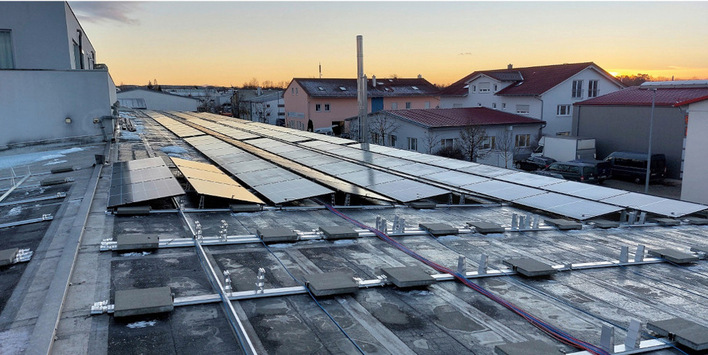 Reihen von Solarmodulen auf einem Dach bei Sonnenuntergang, im Hintergrund sind Wohngebäude zu sehen. - © Foto: Q Cells