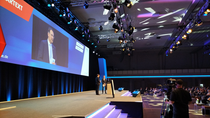 © Tilman Weber VKU-Verbandstagung 2025 in Berlin: VKU-Hauptgeschäftsführer Ingbert Liebing erklärt die Stadtwerkeforderung nach einem „Neustart der Energiewende“. VKU-Präsident Ulf Kämpfer (hinten), Kieler Oberbürgermeister, verweist darauf, dass der „Kanzler in spe“ zur selben Zeit gerade das „Grünen verstehen“ übe.