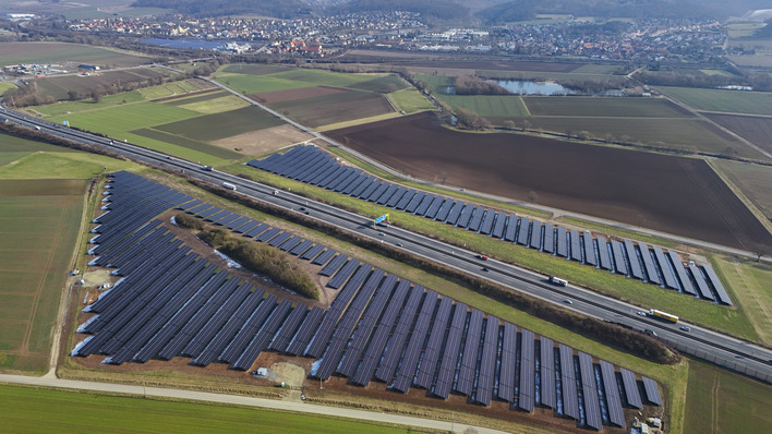 Luftaufnahme von Solarmodulen neben einer Autobahn mit Feldern und Städten im Hintergrund. - © Hamburger Energiewerke
